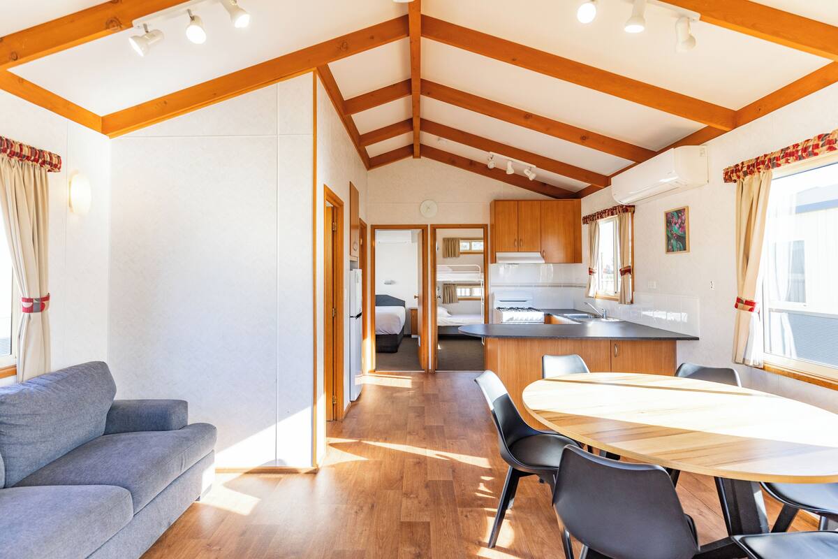 Una habitación amplia con techo de madera, una mesa de comedor con sillas, un sofá y una zona de cocina con armarios y un lavamanos.