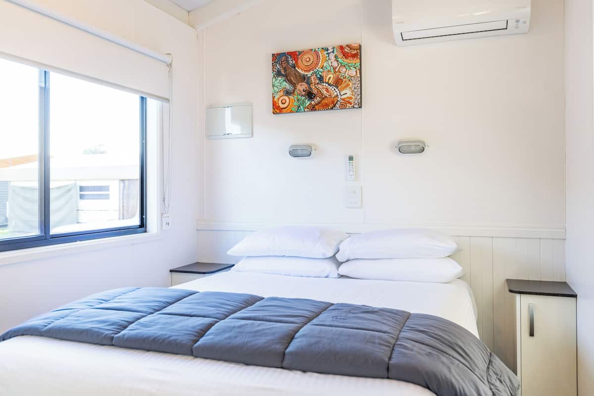 Habitación de hotel con cama, ventana, aire acondicionado, termostato y una obra de arte colgada en la pared.