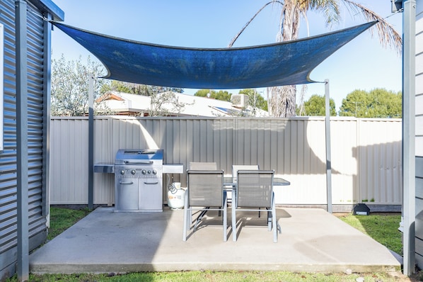 A backyard with a barbecue grill, two metal chairs, and a blue canopy.