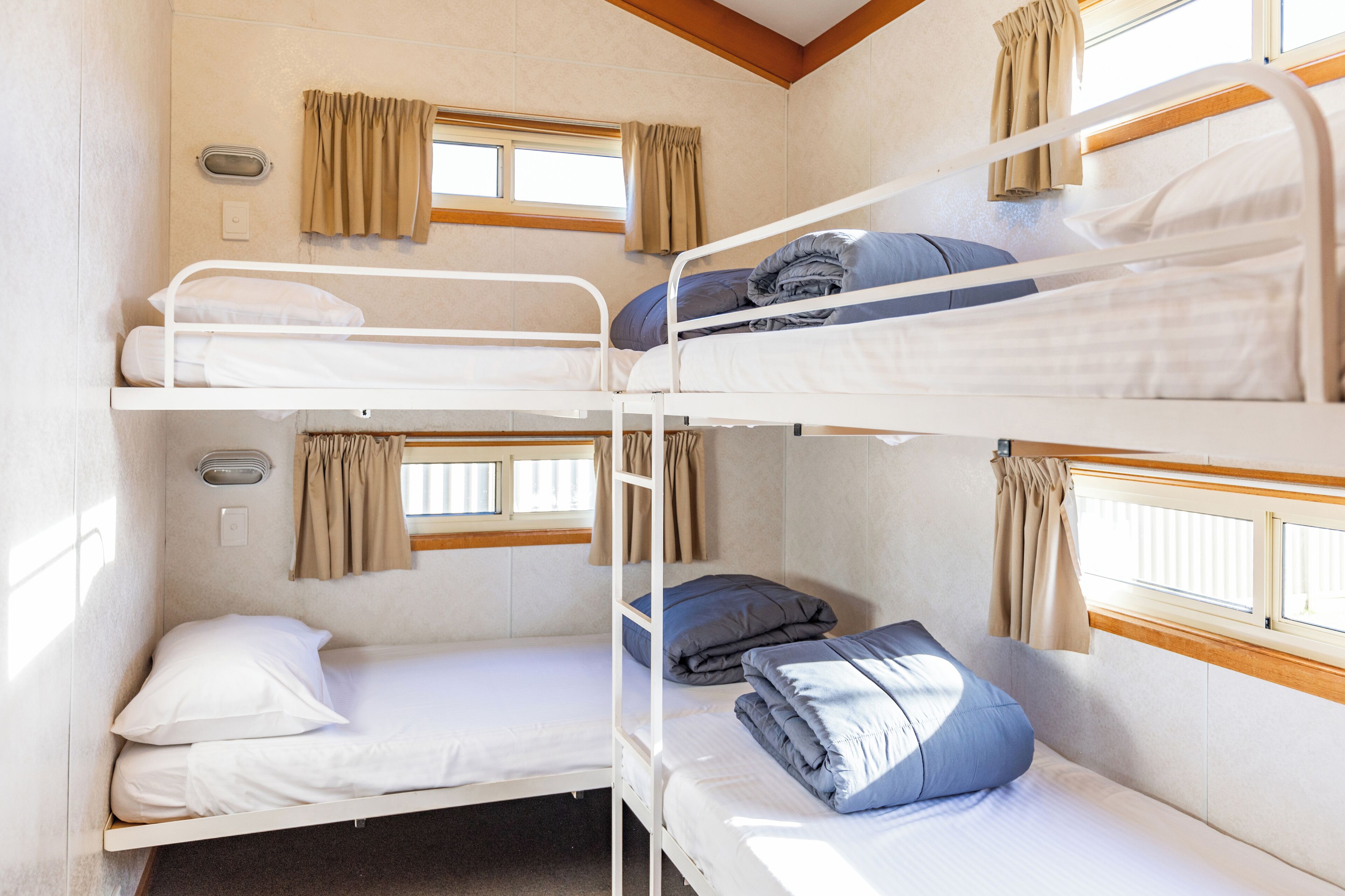 A bunk room with three beds, each with pillows and blankets, and a window with curtains.