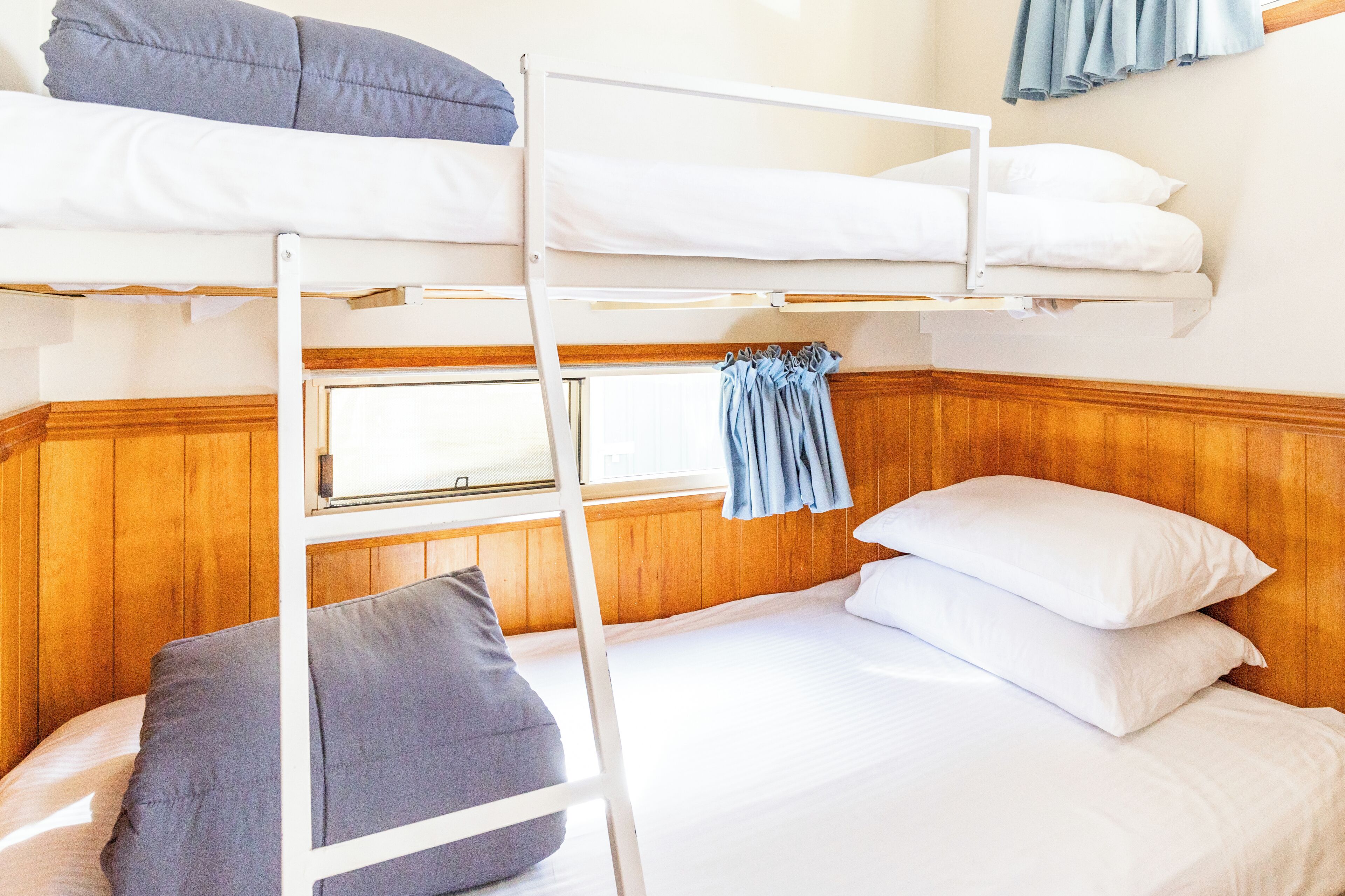 A bunk bed room with a wooden wall, a window with curtains, and a ladder.