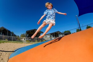 Niño saltando en un tobogán de colores, con un cielo azul despejado y casas al fondo.
