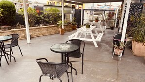 An outdoor patio area with round tables and chairs, surrounded by potted plants and a decorative fence. - Buccaneer Motel Pet friendly (Long Jetty)