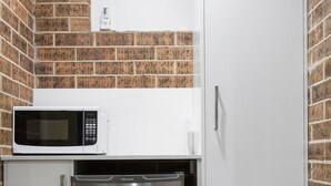 A compact kitchen with a microwave, a stainless steel refrigerator, and a white cabinet. - Buccaneer Motel Pet friendly (Long Jetty)