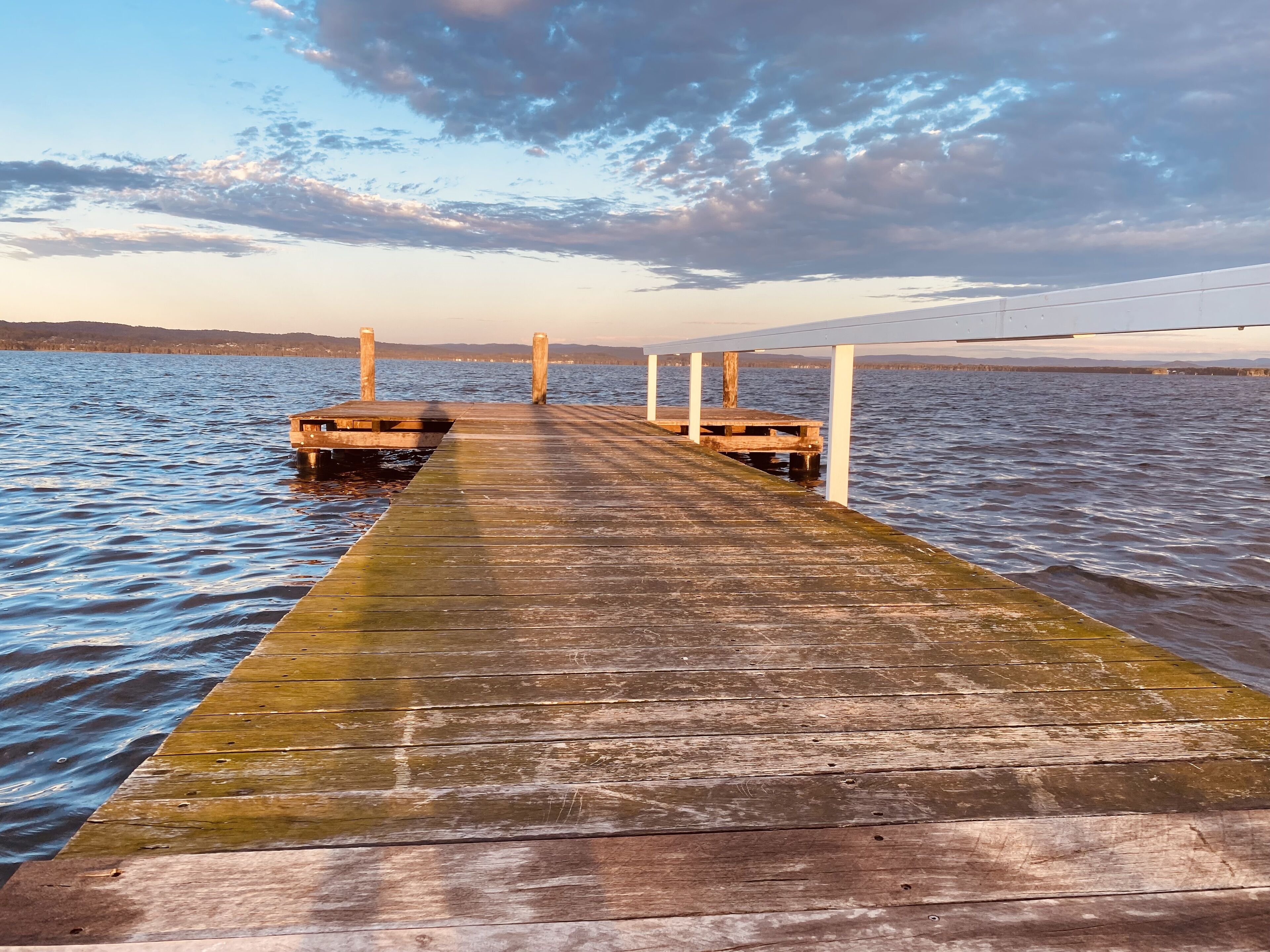 Eine Holzstege, der sich in ruhiges Wasser erstreckt, mit blauem Himmel darüber.