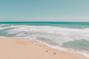 A beach with people walking along the shore and the ocean in the background. - Buccaneer Motel Pet friendly (Long Jetty)