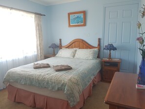 A bedroom with a bed, two nightstands, a wooden door, a framed picture on the wall, and a vase with flowers on a table. - Lake Front Motel (The Entrance North)