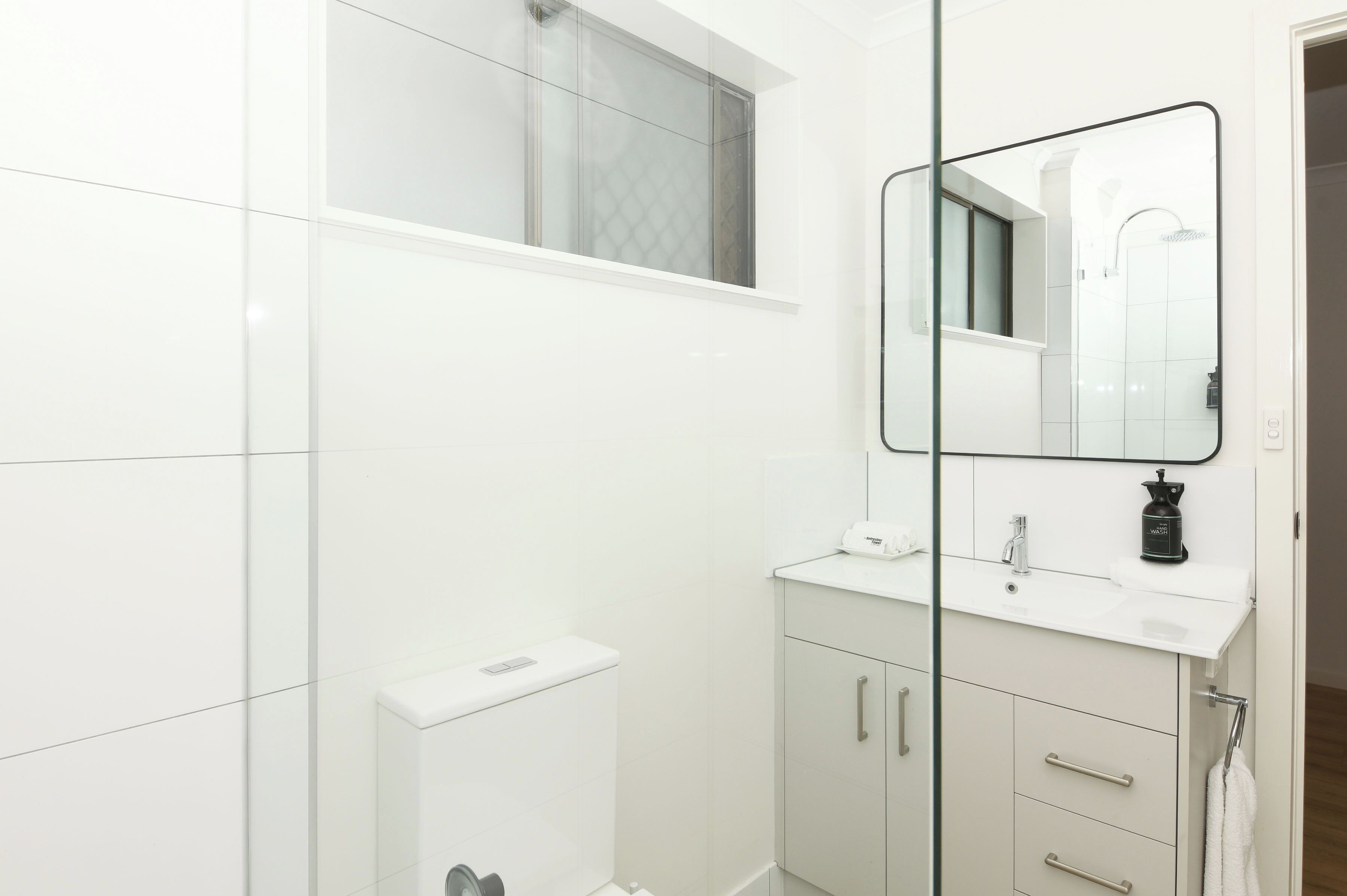 A modern bathroom with a white vanity, a mirror, and a shower area.