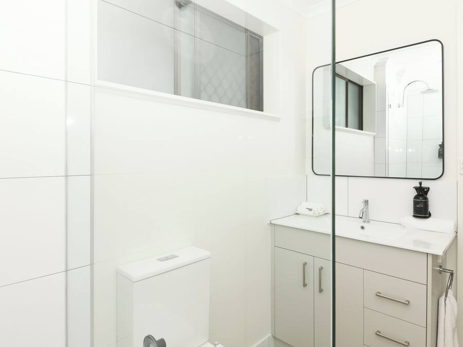A modern bathroom with a white vanity, a mirror, and a shower area.