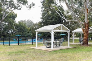 A covered outdoor seating area with tables and chairs, a pool, and a fenced pool area. - Greenacres Motel (Corowa)