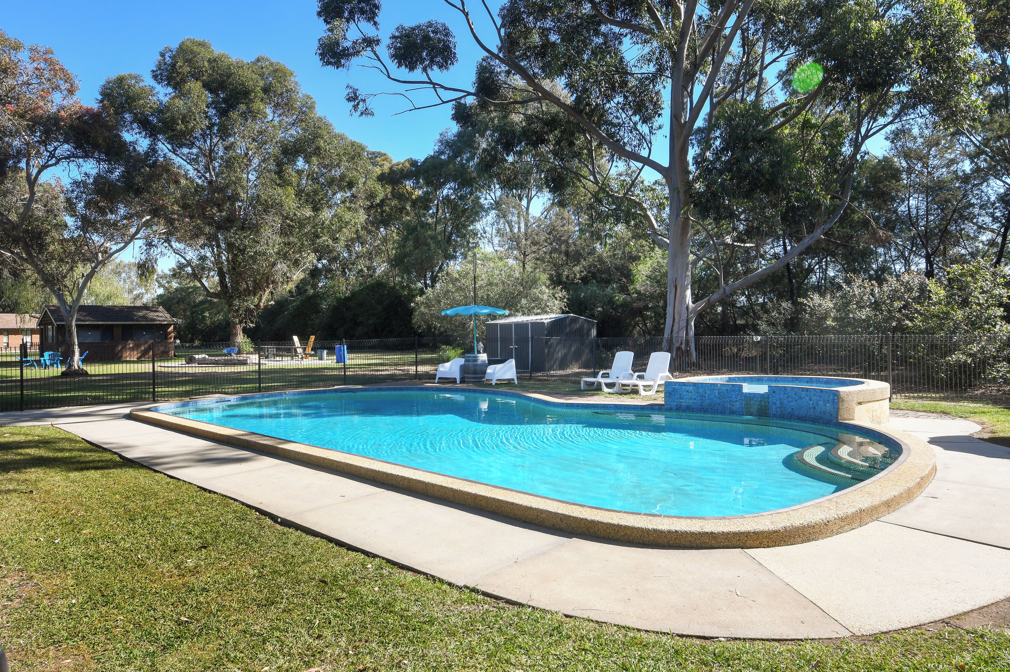 A rectangular swimming pool with a tiled edge, surrounded by a grassy area and a fence.