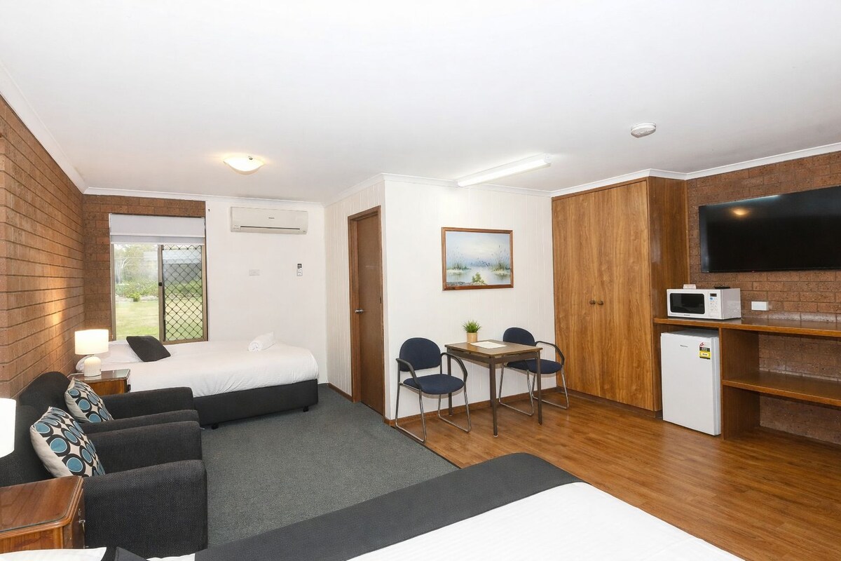 A hotel room with a bed, a seating area with a table and chairs, a kitchenette with a microwave, and a TV on the wall.
