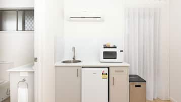 Une petite cuisine équipée comprenant un réfrigérateur, un four à micro-ondes, un évier et une petite poubelle.