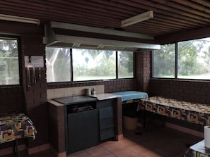 Un pequeño rincón de cocina con pared de ladrillo, una ventana y una mesa cubierta con mantel estampado.