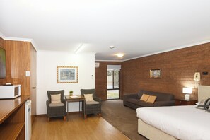 A hotel room with a bed, two armchairs, a small table, a microwave, a TV, and a brick wall. - Greenacres Motel (Corowa)