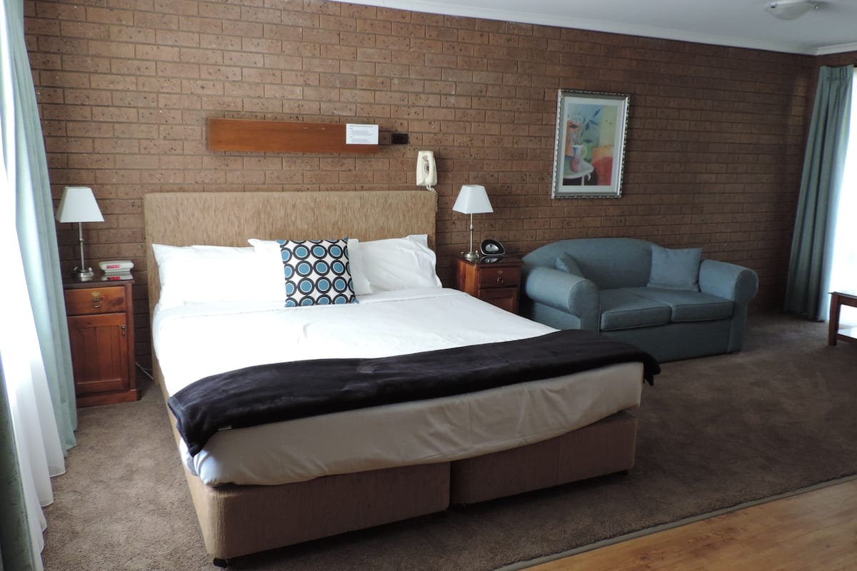 A hotel room with a large bed, a chair, a desk, and a brick wall.