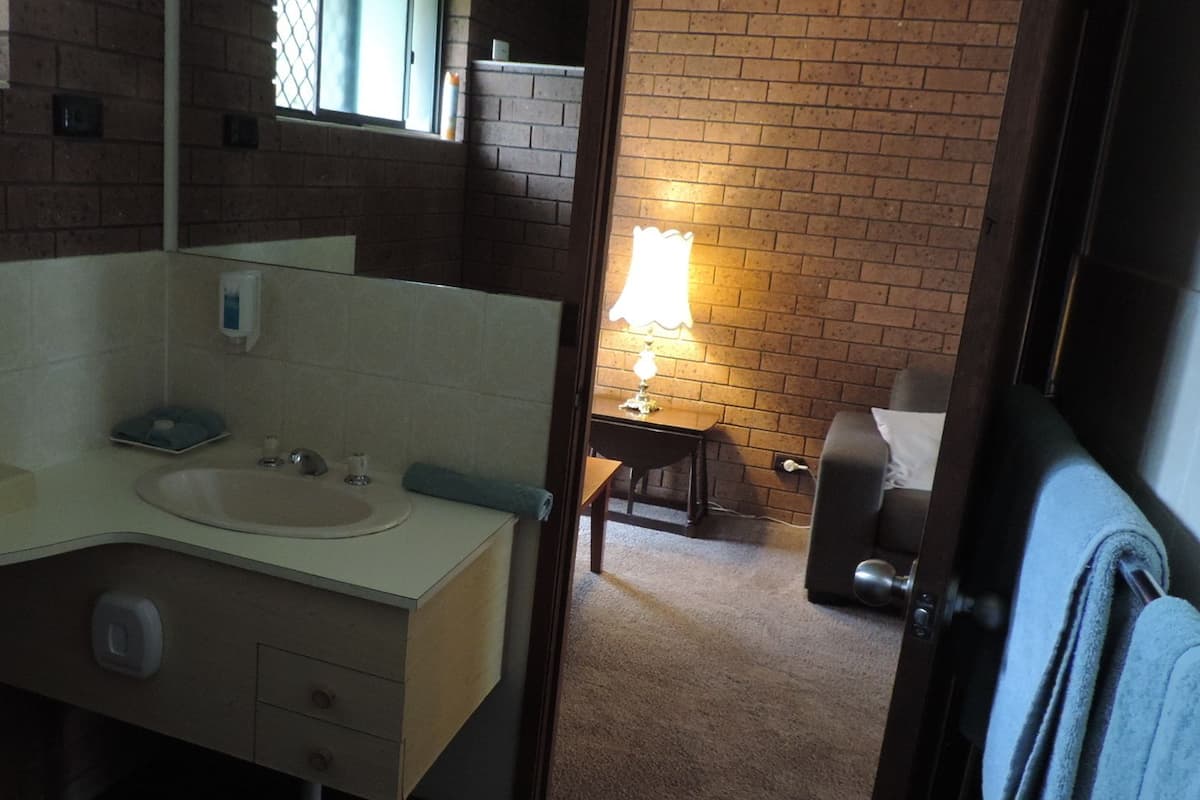 A bathroom with a sink, mirror, and a small table with a lamp.