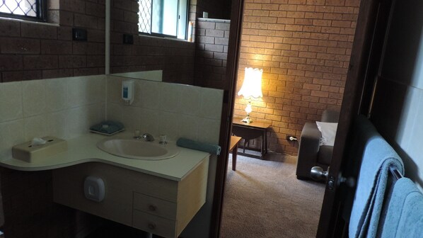 A bathroom with a sink, mirror, and a small table with a lamp. - Greenacres Motel (Corowa)