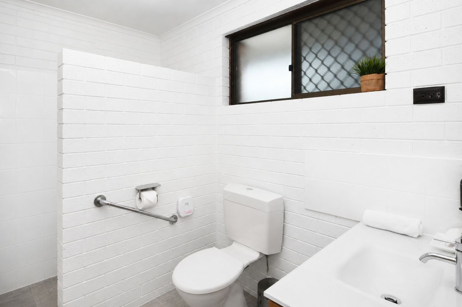 A modern bathroom with white subway tiles, a toilet, a sink, and a window with a plant.