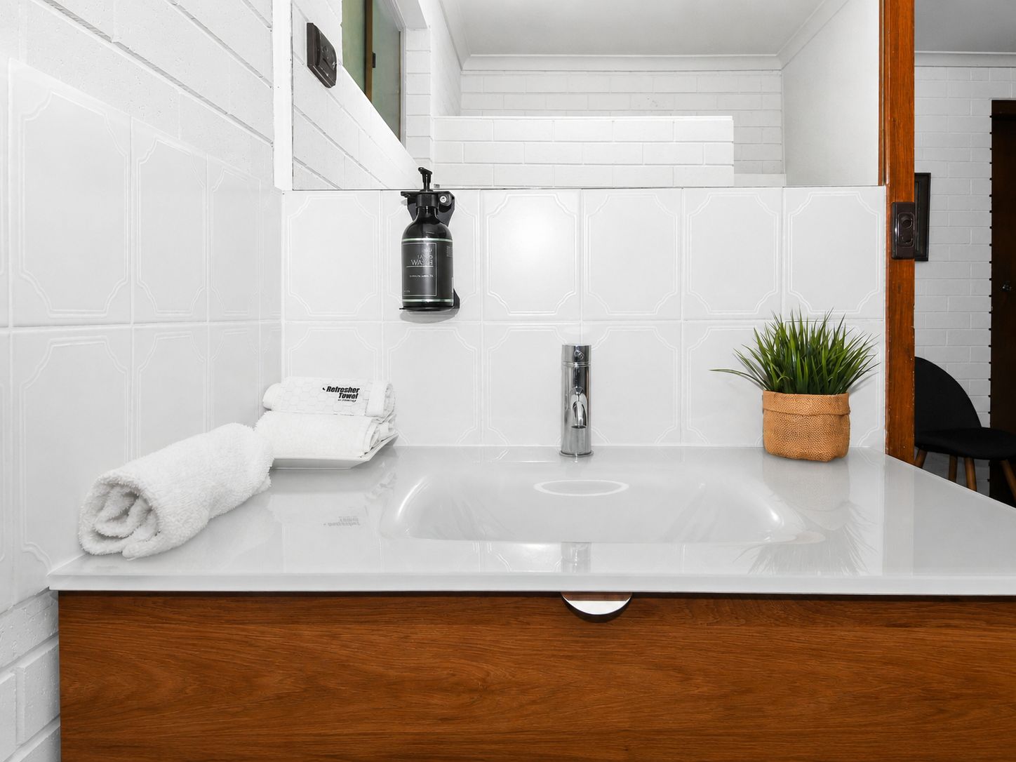 A bathroom with a white sink, a towel, a plant, and a mirror.