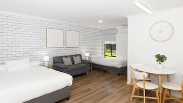 A hotel room with a brick-patterned wall, a large bed, a sofa, a smaller bed, a dining table with chairs, and a potted plant.
