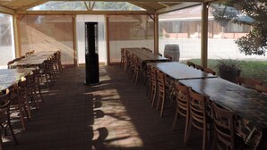 Un área de comedor al aire libre cubierta con varias mesas y sillas, un pilar central y vistas del entorno.