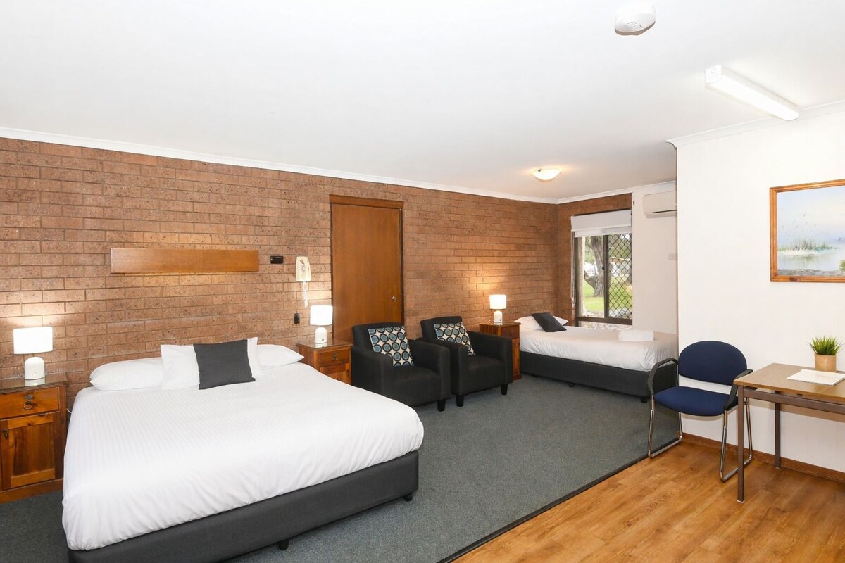 A hotel room with two beds, a desk, a chair, and a window with a view.