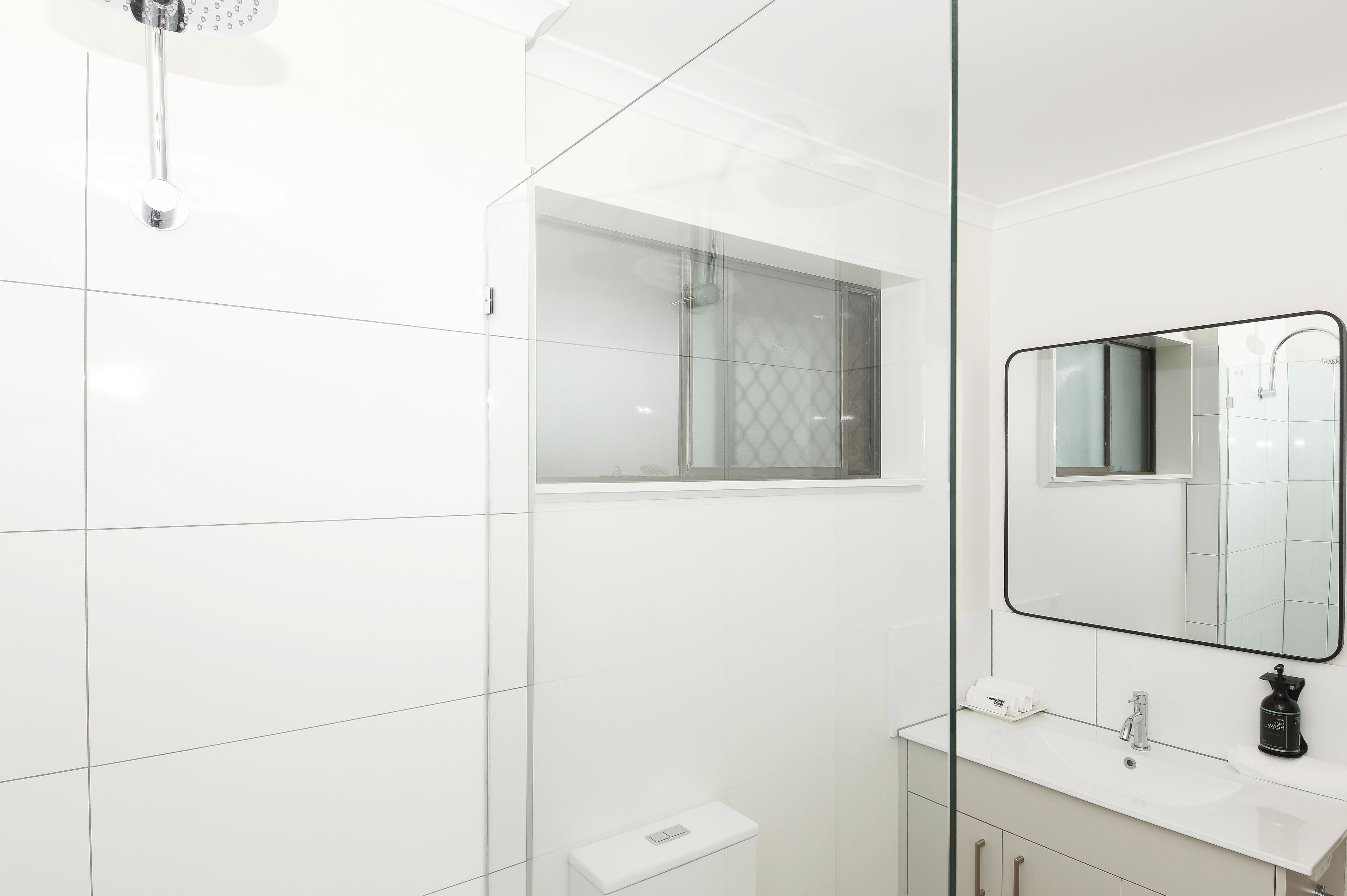 A modern bathroom with a glass shower enclosure, a white sink, and a mirror.