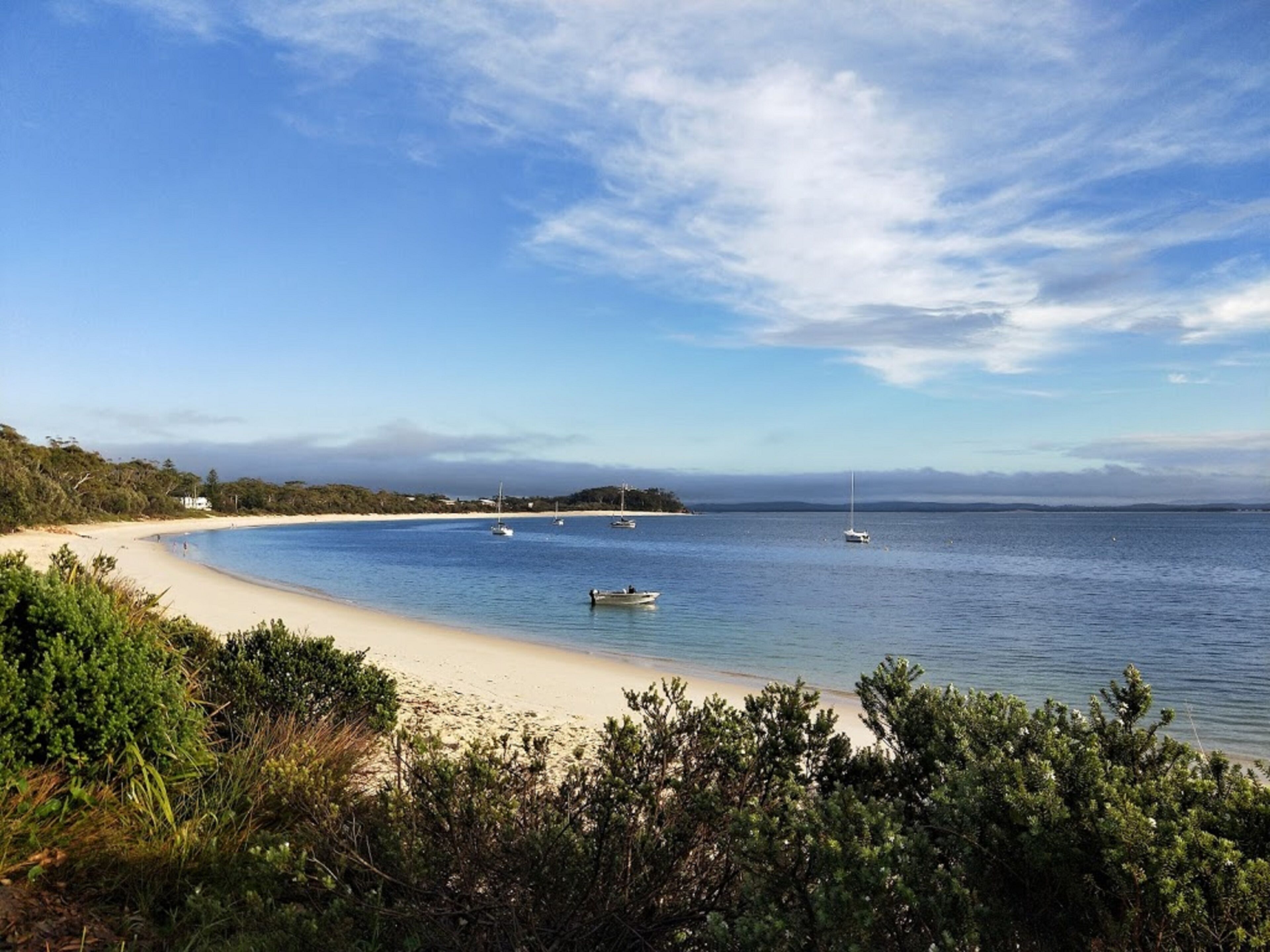 Una playa con cielos despejados, agua tranquila y barcos.