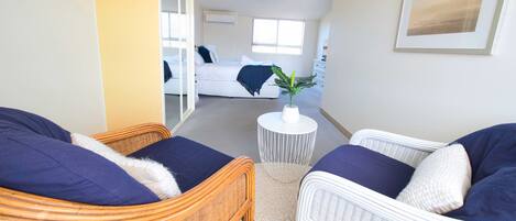 Una habitación con muebles de mimbre, una mesita blanca con una planta y una cama con una colcha azul.