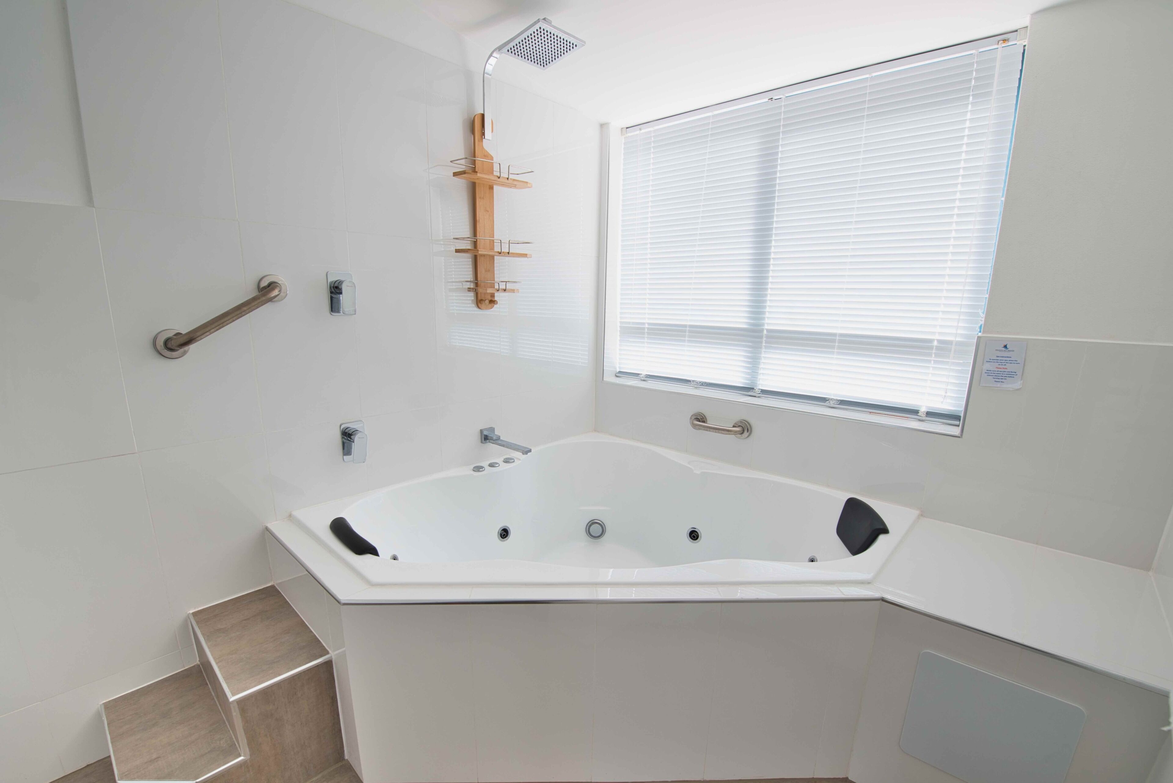 Une salle de bain moderne avec une baignoire sur pieds, une pomme de douche, une fenêtre avec stores et une barre d’appui.