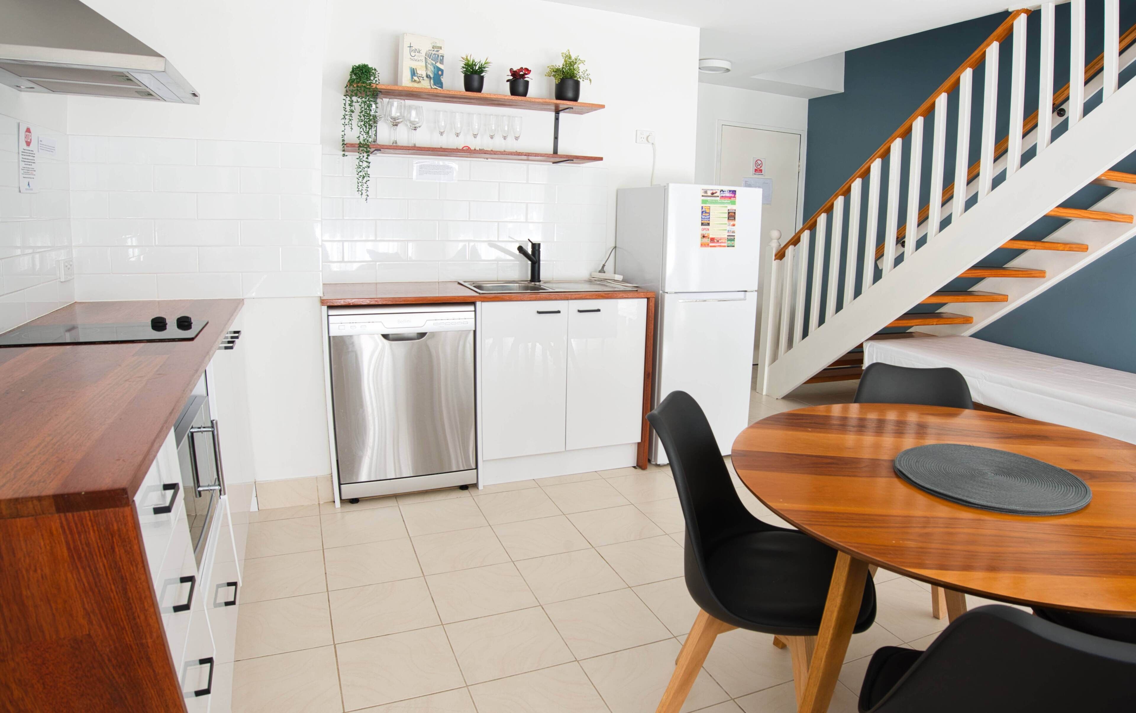 A modern kitchen with white cabinets, a dishwasher, and a wooden dining table with black chairs.