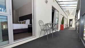 A corridor with a bed, a table, and chairs, leading to a room with a bed and a window. - Quality Suites Amore (Christchurch)