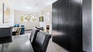 A conference room with a large table, several chairs, a dark wooden wardrobe, and a window with a view of trees. - Quality Suites Amore (Christchurch)