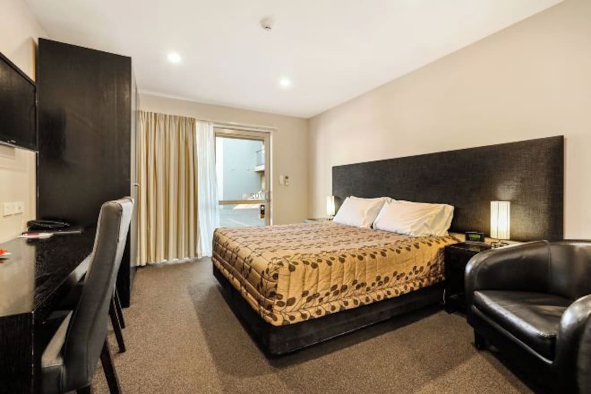 A hotel room with a bed, a desk, a chair, and a TV.