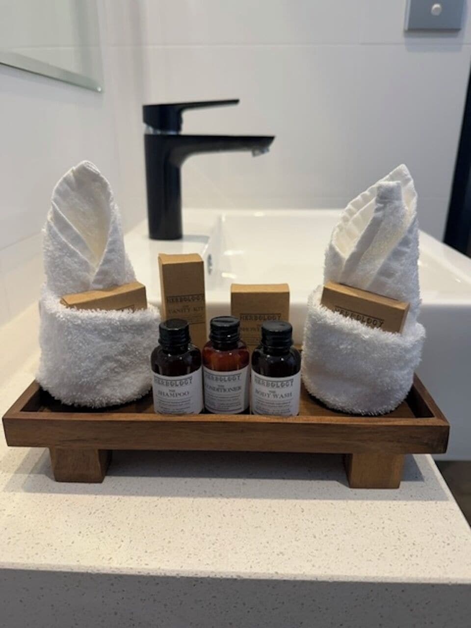 A bathroom with a wooden tray holding toiletries, towels, and a bottle of shampoo.