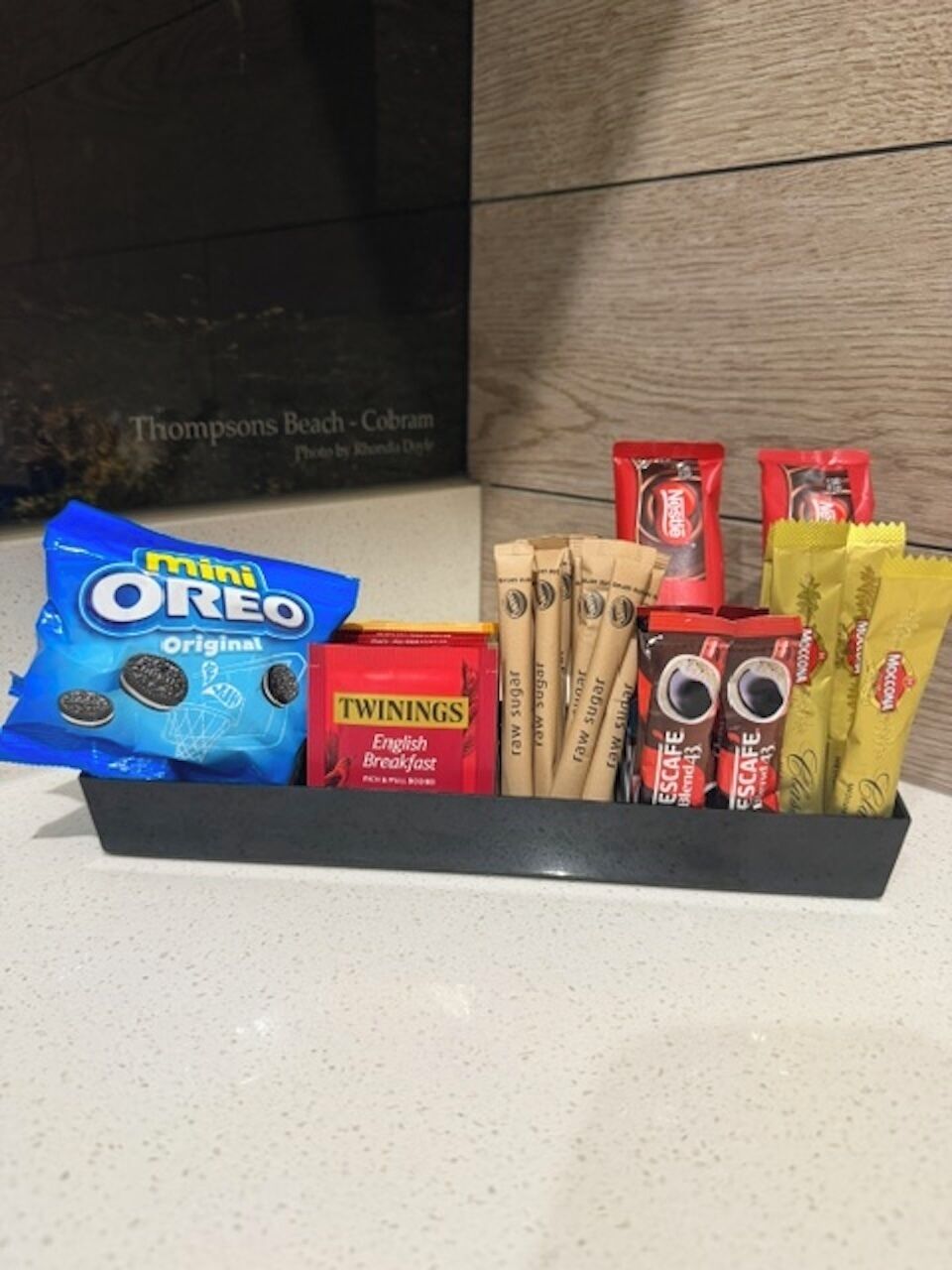 Un plateau noir contenant divers en-cas, notamment des mini-biscuits Oreo, du thé English Breakfast de la marque Twinings, des sachets de sucre brut et un mélange de thé appelé Escape.