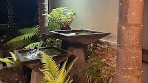 A water feature with a stone basin, surrounded by ferns and plants, against a wall with string lights. - Barooga River Gums Motor Inn (Barooga)