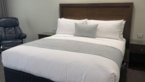 A hotel room with a large bed, a wooden headboard, a chair, and a nightstand. - Barooga River Gums Motor Inn (Barooga)