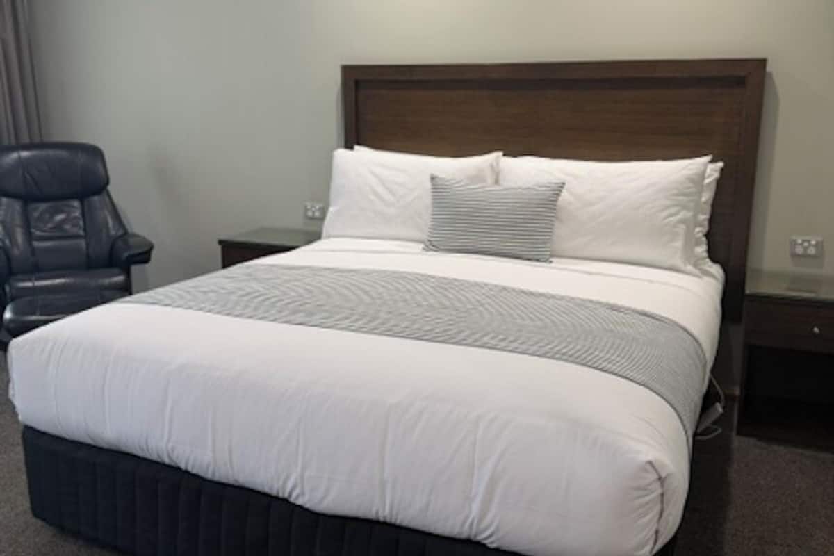 A hotel room with a large bed, a wooden headboard, a chair, and a nightstand.