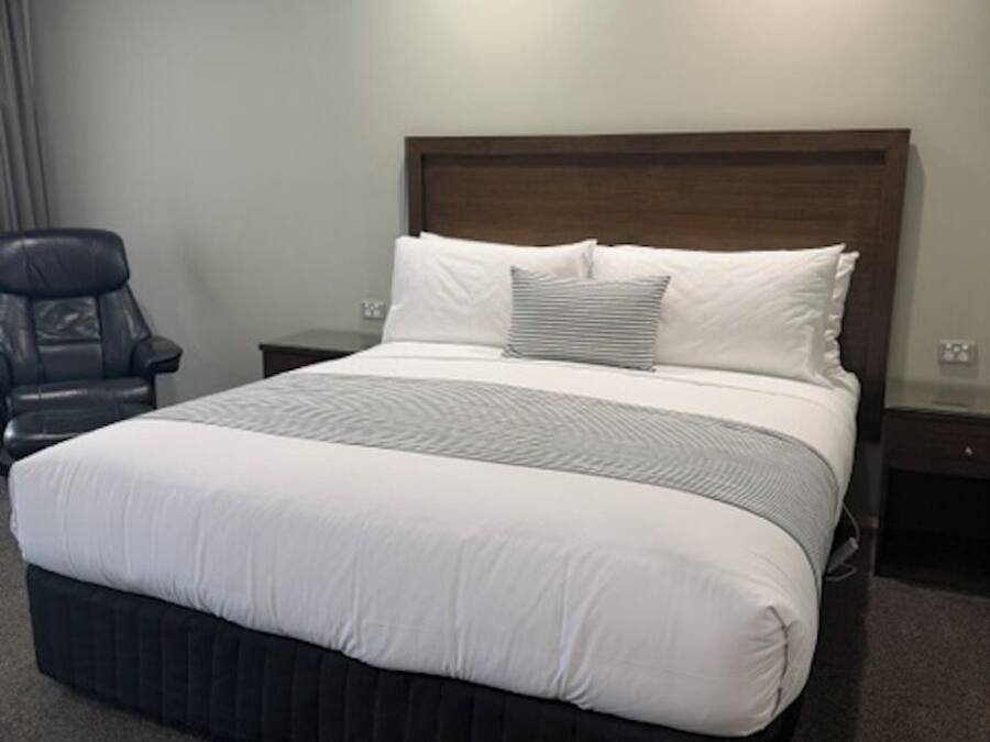 Ein Hotelzimmer mit einem großen Bett, einem Holzkopfende, einem Stuhl und einem Nachttisch.