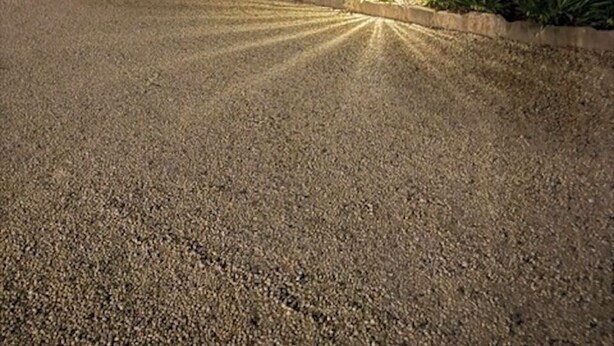 A gravel driveway leading to a building with a garage, surrounded by palm trees and well-lit landscaping. - Barooga River Gums Motor Inn (Barooga)