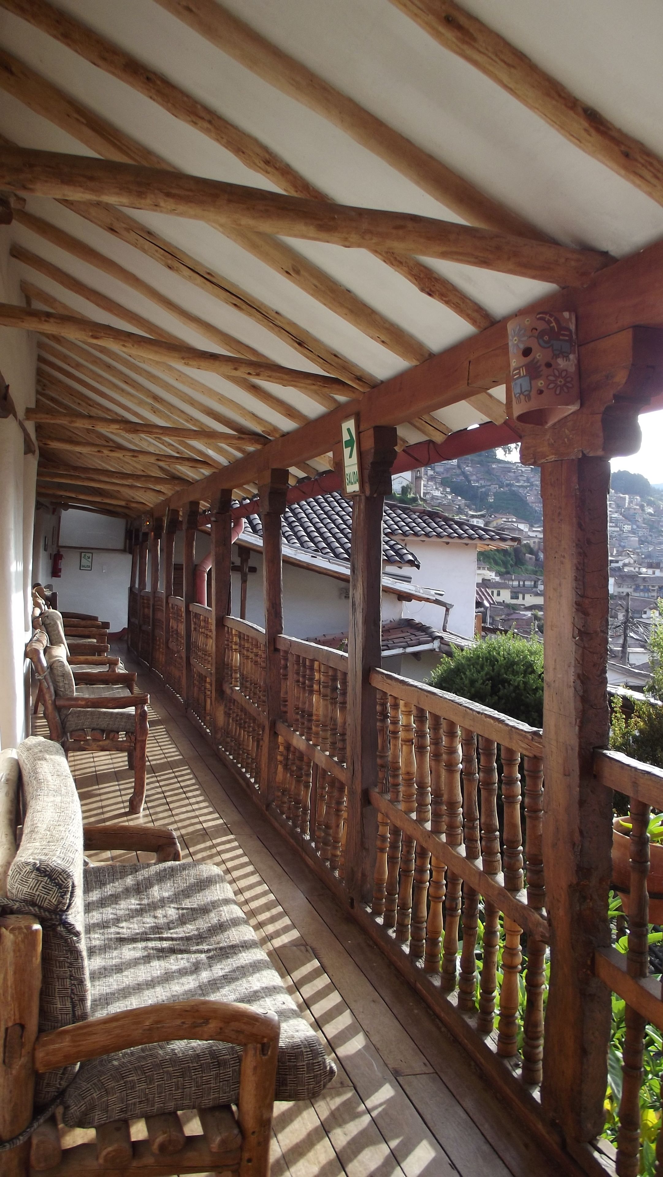 A covered balcony with wooden railings and several cushioned chairs.