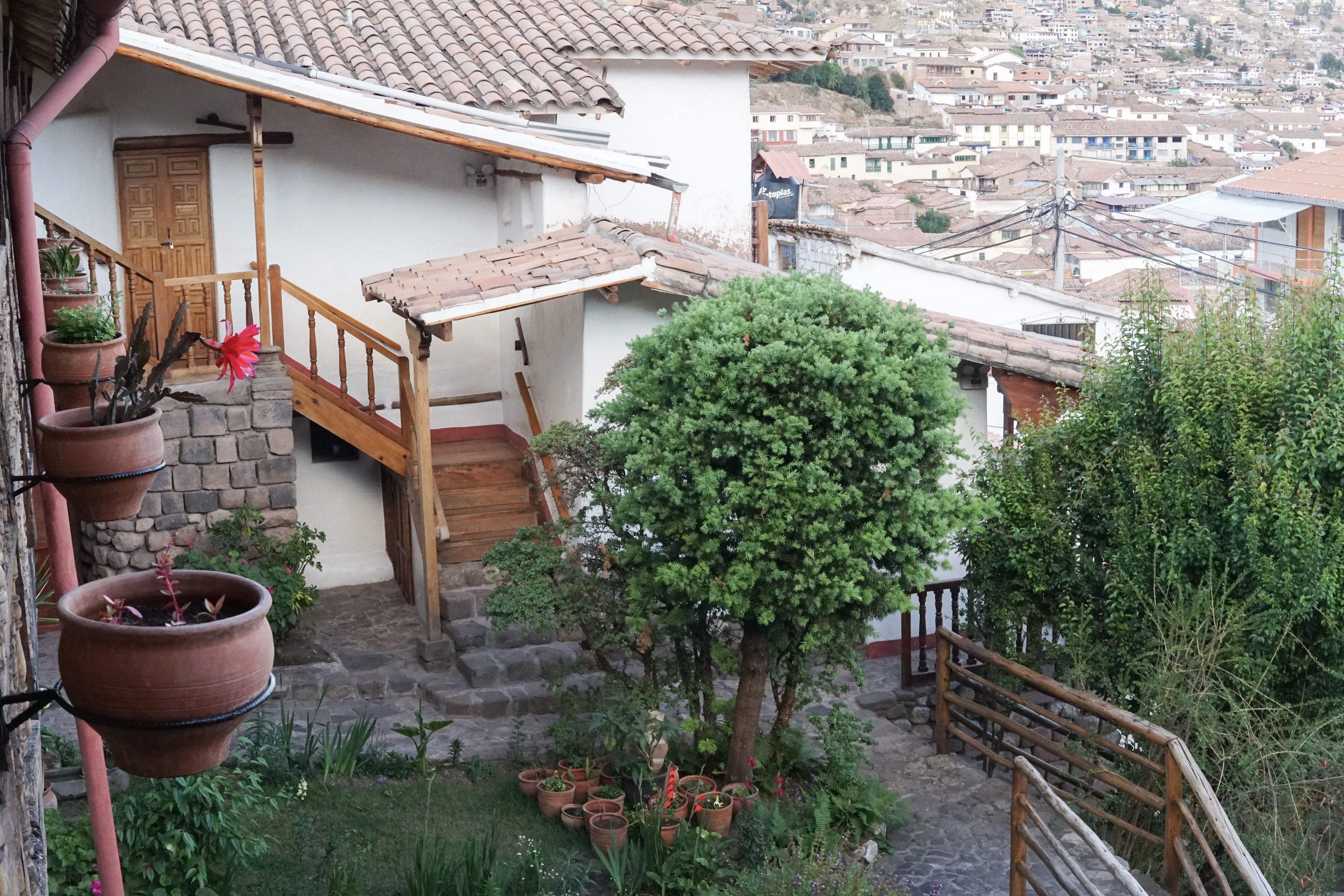 A courtyard with a wooden staircase, potted plants, and a view of a hillside town.