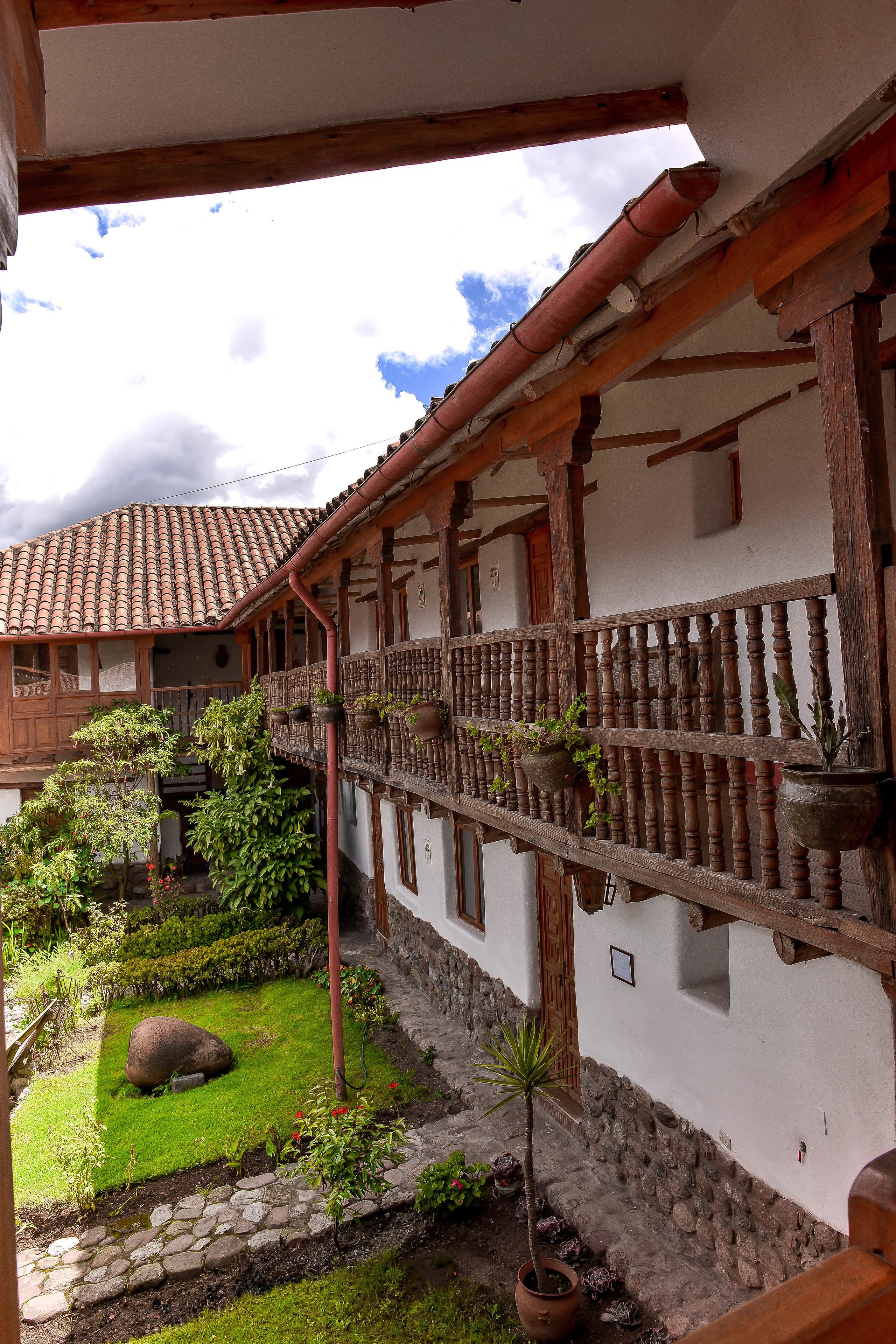 Un edificio tradicional con balcón, sendero de piedra y plantas en macetas.