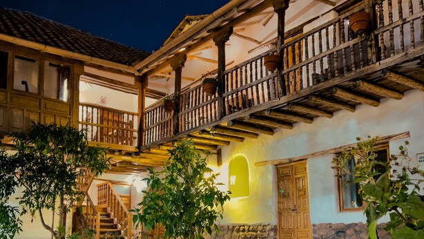 Un cortile rustico con una panchina in legno, un muro in pietra e una scala che conduce a un balcone.