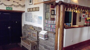 A rustic interior with a stone wall, a wooden bench, a cash register, and a 'SALIDA' sign.