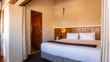 A bedroom with a bed, wooden beams, a hanging light fixture, and a door.