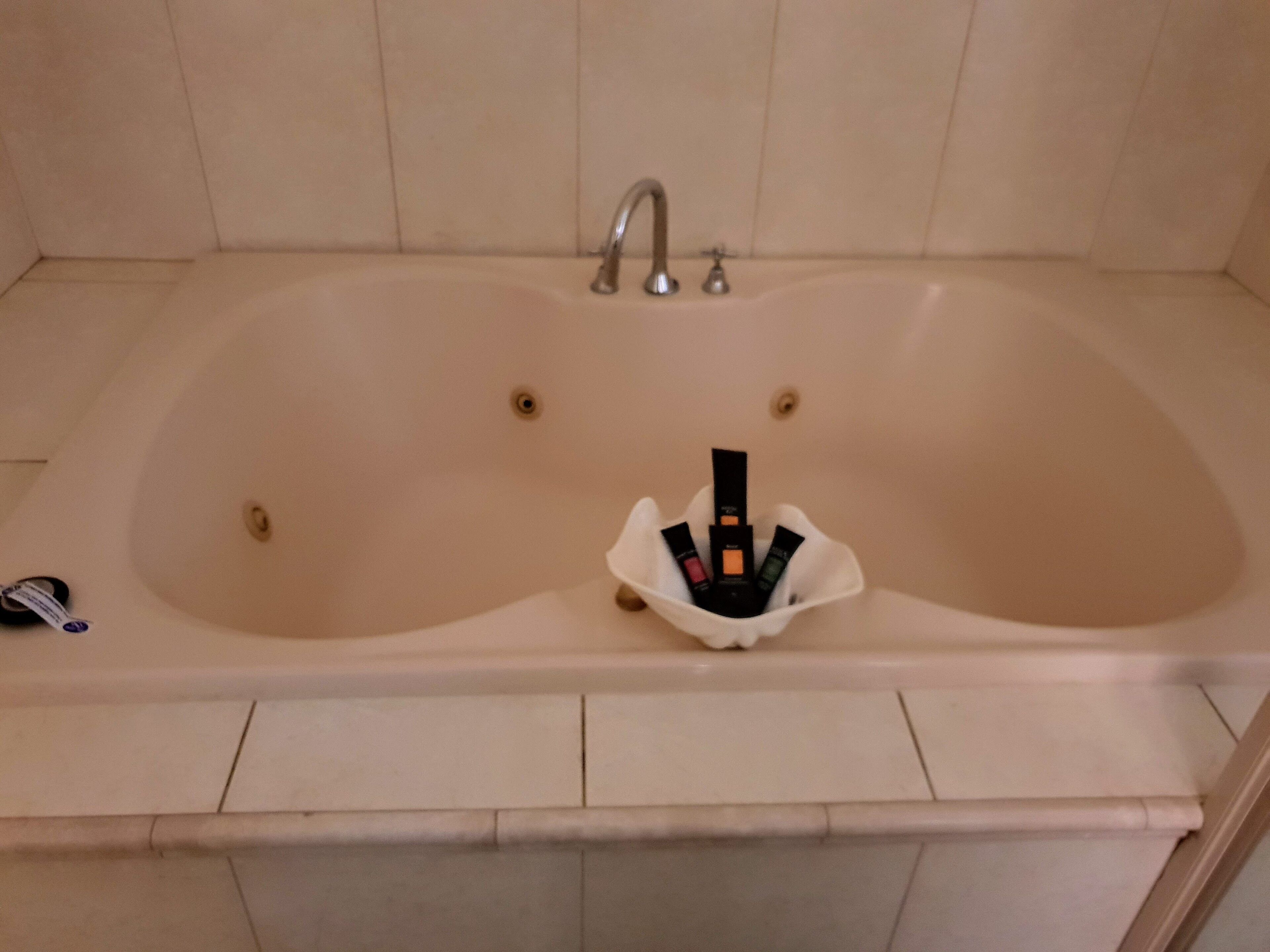 A large, empty bathtub with a faucet and a small shelf with toiletries.