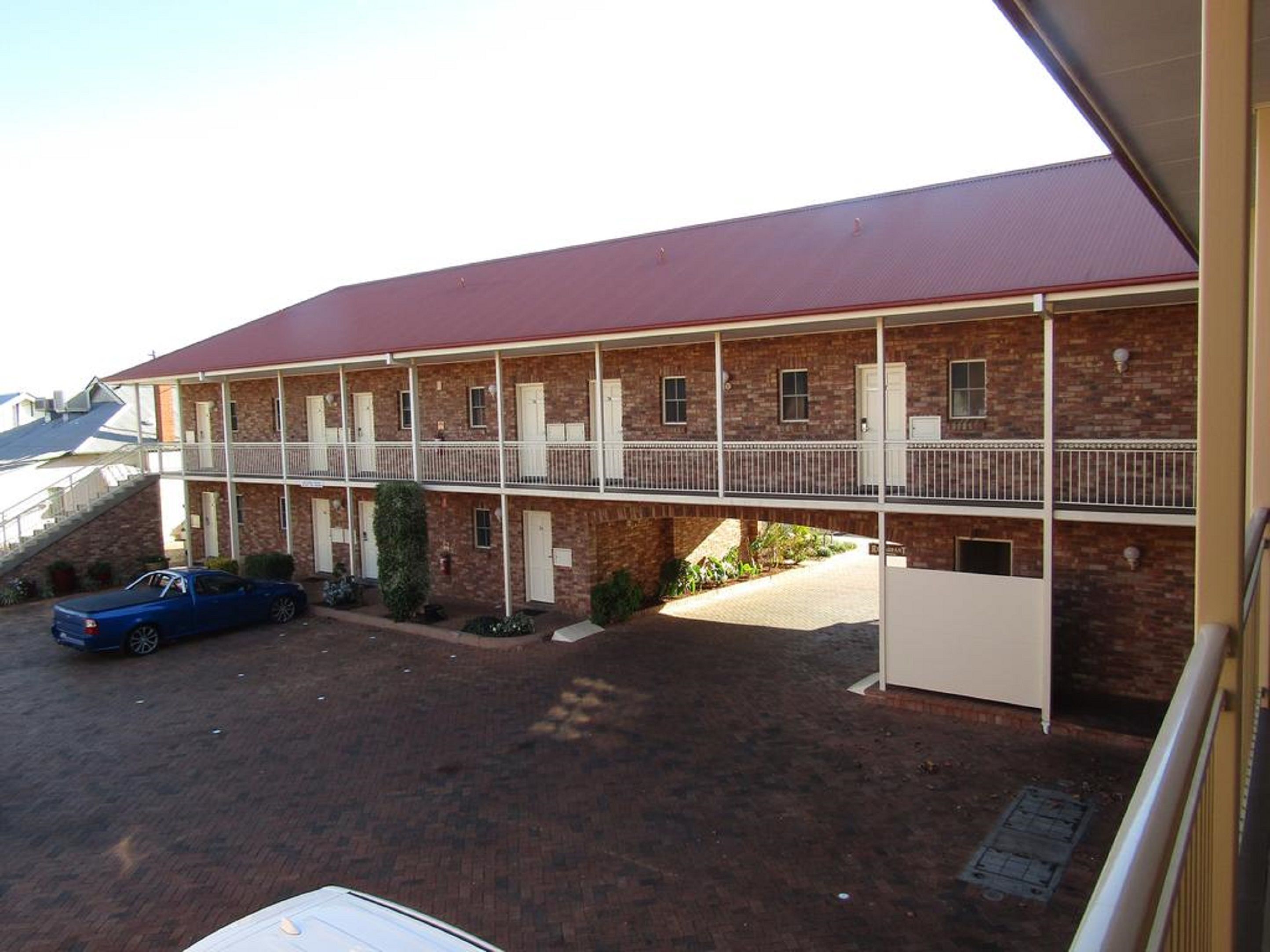 Un motel de dos pisos con techo rojo, fachada de ladrillo y zona de estacionamiento cubierta.